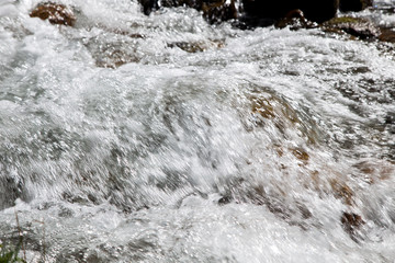 Water in the mountain raging river. Beautiful natural background of stones and water. Texture of clear water and fast river.