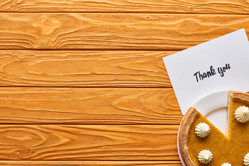 top view of pumpkin pie and thank you card on wooden table