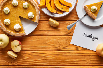 top view of pumpkin pie, ripe apples and thank you card on wooden table