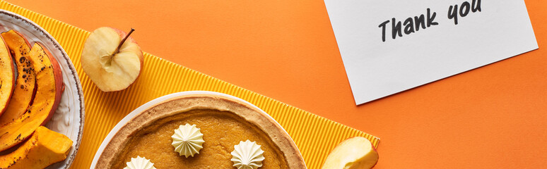 panoramic shot of delicious pumpkin pie with thank you card on orange background with apples