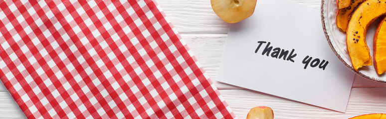 top view of pumpkin, ripe apples and thank you card on wooden white table with plaid napkin, panoramic shot