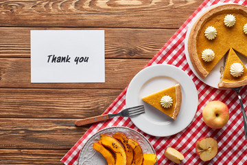 top view of pumpkin pie, ripe apples and thank you card on wooden brown table with red plaid napkin