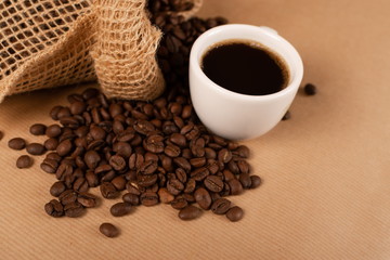 Hot coffee cup and coffee beans on brown background closeup