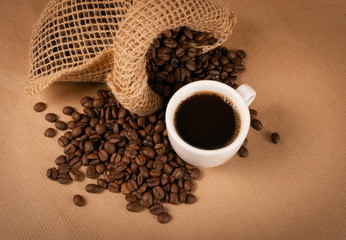 Hot coffee cup and coffee beans on brown background closeup
