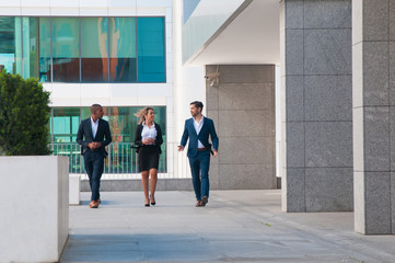 Successful team discussing project on their way to office. Business men and woman walking near office building an talking. Confident team concept