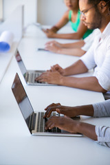 Diverse group of people using digital devices in workspace. Man and women sitting at long desk, working on laptops and tablets. Digital communication concept