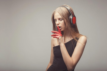 Fashion pretty girl listening music with headphones, wearing red gloves, take pleasure with song, and ask everybody to shut up, using her finger near mouth. Lifestyle woman concept