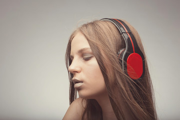 Fashion pretty girl listening music with headphones, wearing red gloves, close eyes and take pleasure with song
