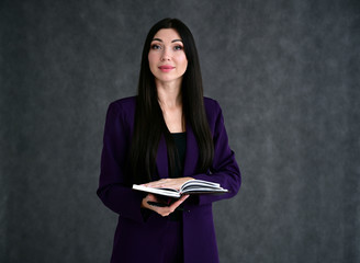Portrait of a pretty brunette girl with good makeup with long hair on a gray background in a business suit with a folder in her hands. Stands in different poses with emotions.
