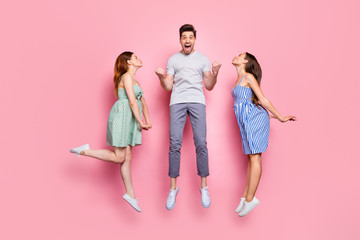 Full size profile side photo of screaming person with raised fists and charming ladies kissing him wearing striped t-shirt pants isolated over pink background