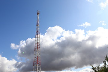 Telecommunications tower on light blue sky background and white club clouds