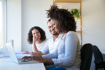 Happy colleagues chatting and joking while working on project. Man and women sitting at workplace...