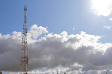 Obraz premium Telecommunications tower on light blue sky background and white club clouds