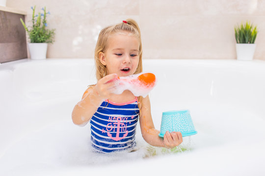 Little blonde girl taking bubble bath in beautiful bathroom.Kids hygiene. Shampoo, hair treatment and soap for children. Kid bathing in large tub.