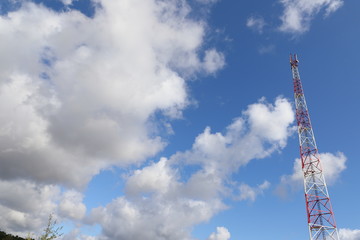 Obraz premium Telecommunications tower on light blue sky background and white club clouds
