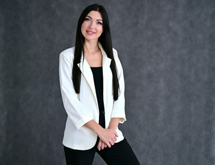 Portrait of a pretty brunette girl with good makeup with long hair on a gray background in a light business suit. Stands in different poses with emotions.