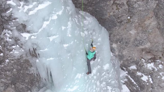 AERIAL: Woman carefully placing her ice-picks while climbing up an icy waterfall. Spectacular shot of an extreme athlete scaling the icy stream cascading down the rocky cliff in Slovenian mountains
