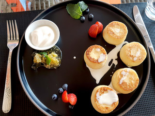 Cheesecakes on a large black plate with sour cream, blueberries, strawberries, a mint leaf and honeycomb