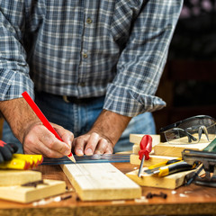 Adult craftsman carpenter with pencil and ruler tracing the cutting line on a wooden table. Housework do it yourself. Stock photography.
