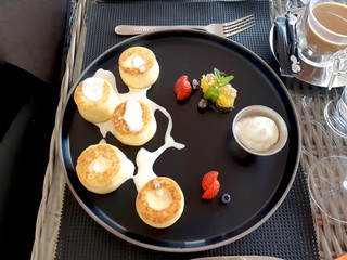 Cheesecakes on a large black plate with sour cream, blueberries, strawberries, a mint leaf and honeycomb