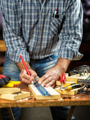 Adult craftsman carpenter with pencil and ruler tracing the cutting line on a wooden table. Housework do it yourself. Stock photography.