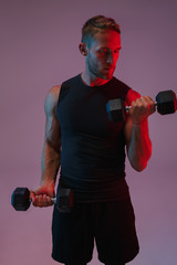 Concentrated young sports man make exercises with dumbbells.
