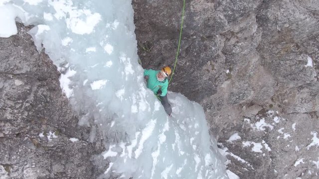 DRONE: Fearless female climber carefully placing her ice-picks while climbing up an icy waterfall. Breathtaking shot of an woman scaling the icy stream cascading down the cliff in Slovenian mountains.