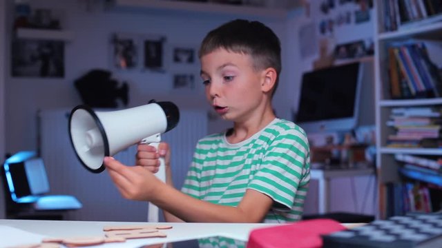 The schoolboy at the table shouts in a megaphone, then begins to play a shootout. Distance school. Online School. Home education during quarantine of coronavirus infection COVID-19.