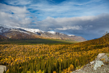 Fototapeta premium View of the autumn forest, mountains and blue sky with white clouds.