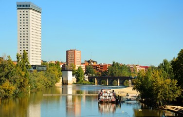 un río, un barco, un puente antiguo y un rascacielos