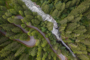 aerial view of a waterfall and a mountain road winding through a fir forest