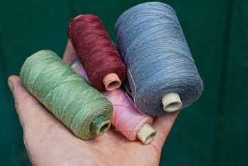 set of bobbins with colored threads on the palm of a hand on a green background