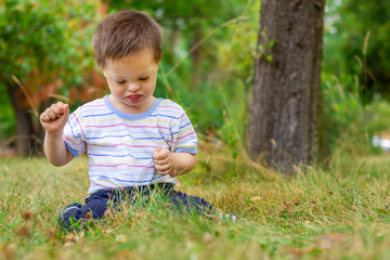 Naklejka na ściany i meble Cute small boy with Down syndrome playing in summer day on nature