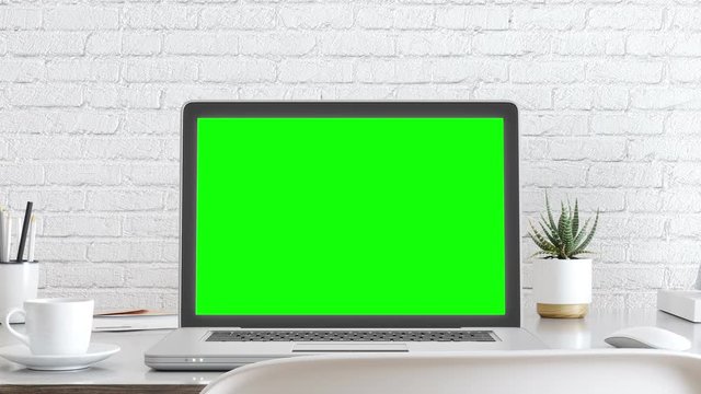 Laptop with blank white screen, and office supplies on a desk with green screen