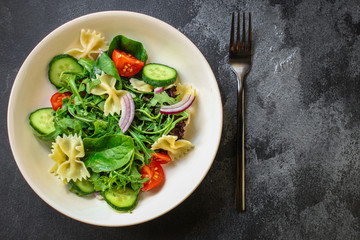 italian pasta salad farfalle, vegetables, mix leaves (tomato, cucumber, onion, lettuce, chard, arugula and more) menu concept. food background. copy space. Top view