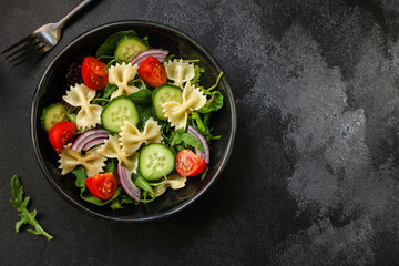 italian pasta salad farfalle, vegetables, mix leaves (tomato, cucumber, onion, lettuce, chard, arugula and more) menu concept. food background. copy space. Top view