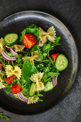 italian pasta salad farfalle, vegetables, mix leaves (tomato, cucumber, onion, lettuce, chard, arugula and more) menu concept. food background. copy space. Top view