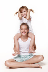 The sister sits on her brother 's neck and pulls herself with her hands by the scallops, everyone laughs, pampers, plays together. In the studio on a white background. Happy childhood.