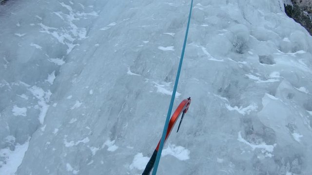 POV: Breathtaking first person view of climbing up a gorgeous frozen waterfall. Climber carefully picking his spots and placing his ice axes into the frozen river cascading down the rocky mountain.