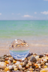 Glass round ball on the beach reflects the sea in summer