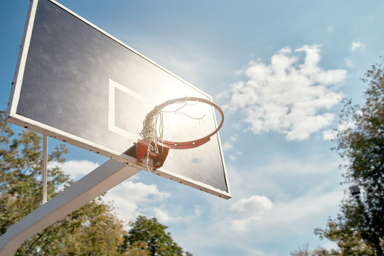 Image of basketball hoop against blue, cloudy sky on summer day.