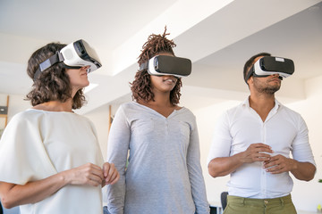 Diverse team of three enjoying VR experience. Man and women wearing virtual reality glasses,...
