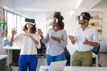 Excited team of three testing VR simulator. Man and women wearing virtual reality glasses, standing...