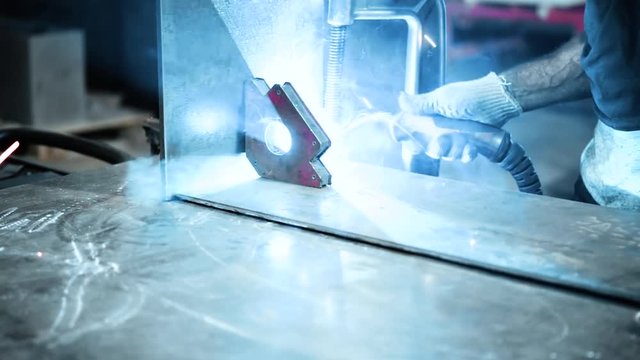 Welder at work. Worker welds metal parts. Welding process, sparks, flame, smoke.