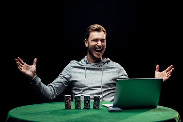 selective focus of happy man gesturing near poker chips near laptop isolated on black