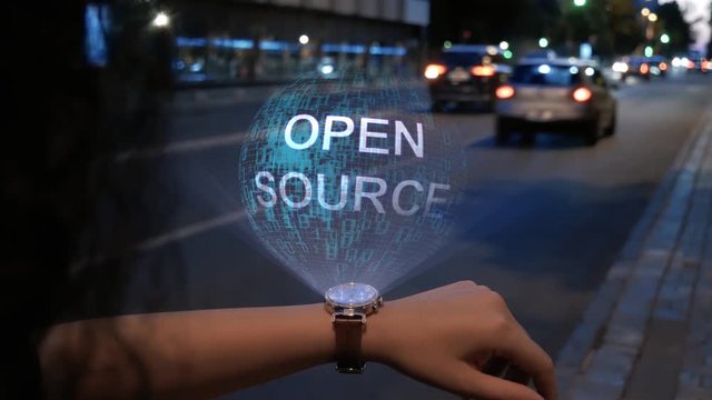 Unrecognizable curly woman with a hologram on smart watch with text Open source. Female hands with future holographic technology on the background of the night road