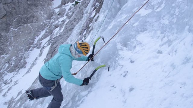 CLOSE UP: Caucasian woman carefully placing her ice axes while climbing up an icy waterfall. Active female traveler goes ice climbing in the beautiful Slovenian mountains. Female alpinist in action
