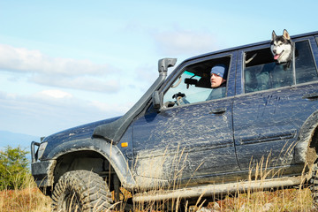 Fototapeta premium Black and white husky rides in a car in the mountains with a man. Carpathian Mountains