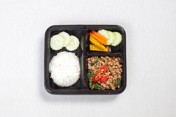 Basil fried rice with minced pork, put in a black plastic box, put on a white tablecloth, food box, Spicy fried pork with basil leaves, Thai food.