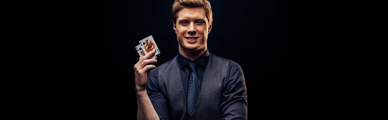 panoramic shot of cheerful man holding playing cards isolated on black